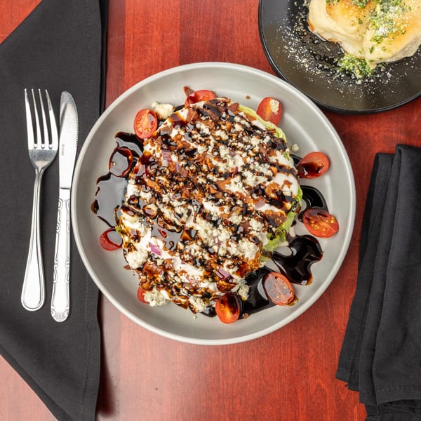 Wedge salad with blue cheese, bacon, tomatoes, and balsamic glaze, next to garlic knots.