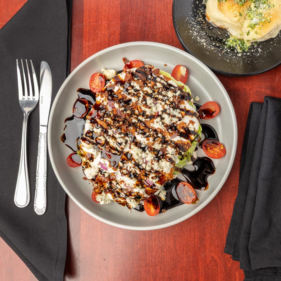 Wedge salad with blue cheese, bacon, tomatoes, and balsamic glaze, next to garlic knots.