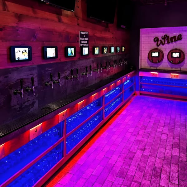 A self-serve beer and wine wall with glowing red and blue lights, screens, and taps.
