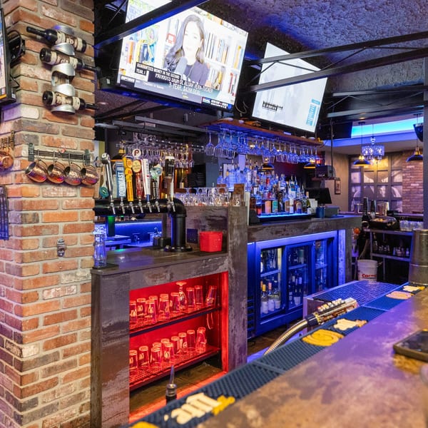 A vibrant bar area at Capo & Co. with blue and red lighting, beer taps, and liquor bottles.