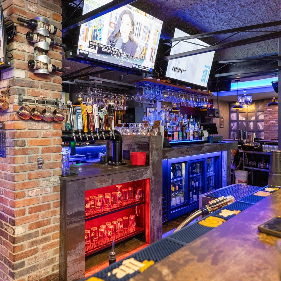 A vibrant bar area at Capo & Co. with blue and red lighting, beer taps, and liquor bottles.