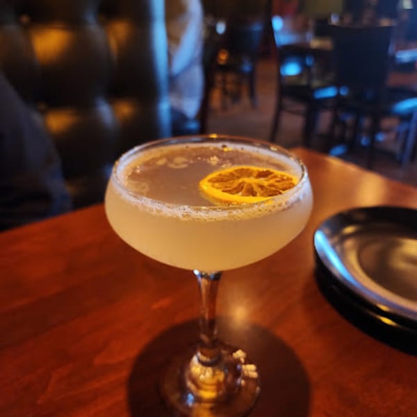 A light-colored cocktail with a dried orange slice, on a wooden table at Capo & Co.