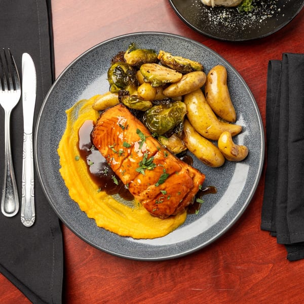 Glazed salmon with butternut squash puree, roasted Brussels sprouts, and fingerling potatoes on a gray plate.