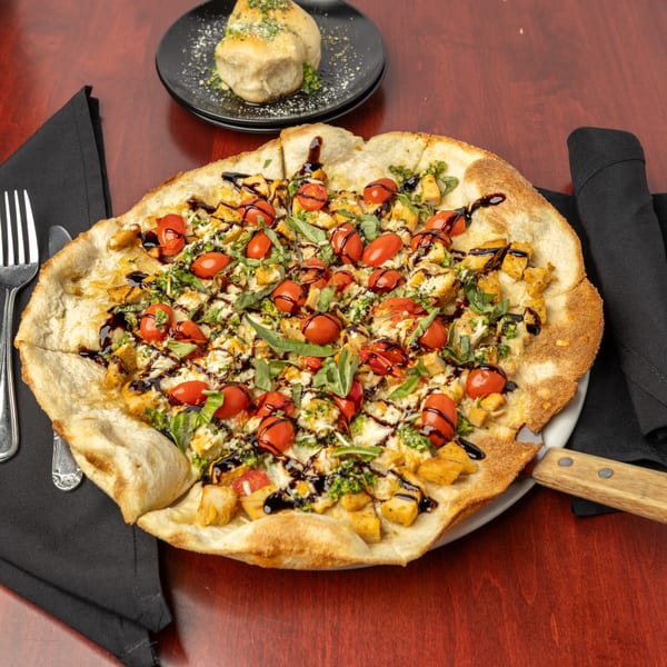 Capo & Co. flatbread pizza with chicken, tomatoes, basil, and balsamic glaze on a wooden table.