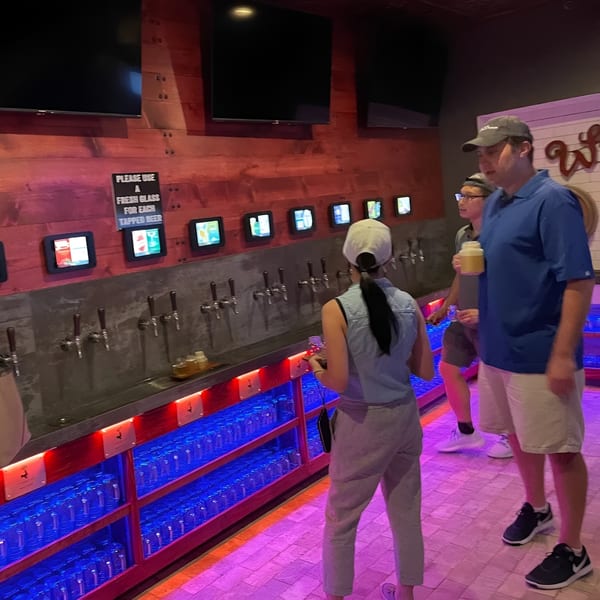 People at Capo & Co. self-serve beer wall with multiple taps, screens, and glowing blue glass storage.