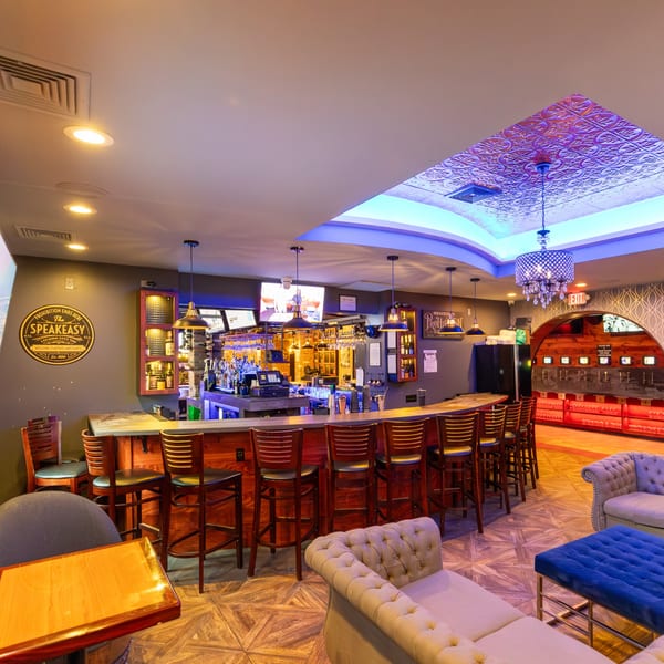 A vibrant bar area with a long wooden counter, bar stools, and a lounge seating area.